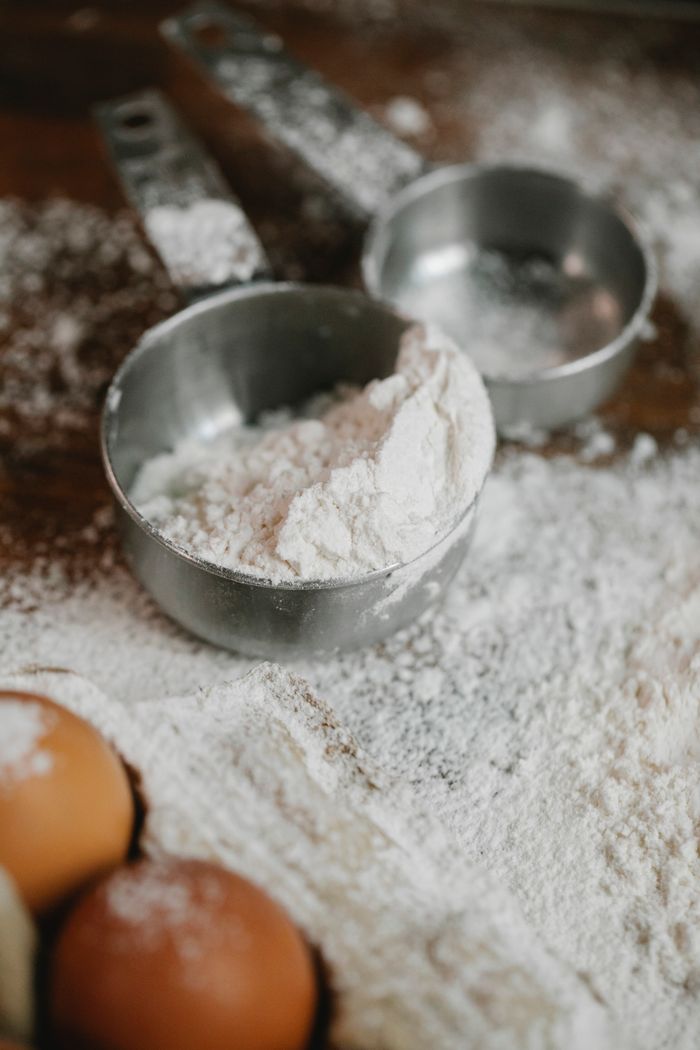High angle of flour in stainless saucepans with eggs on table during baking process